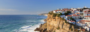 A cliff with houses on top of it near the ocean.